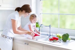 Mother and her daughter washing vegetables with a water heater under the sink